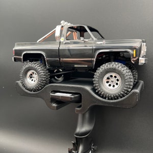 Op de afbeelding: Zwarte en zilveren modeltruck op een zwarte displaystandaard. De truck heeft een rolkooi en een zwart-zilveren lakwerk.