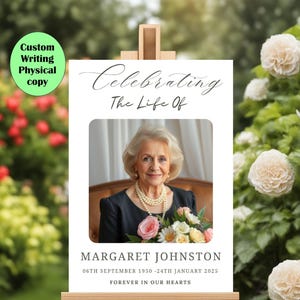 May include: A white easel with a white sign that says "Celebrating The Life Of" with a photo of a woman holding flowers. The text below the photo says "Margaret Johnston 06th September 1950 - 24th January 2025 Forever In Our Hearts."