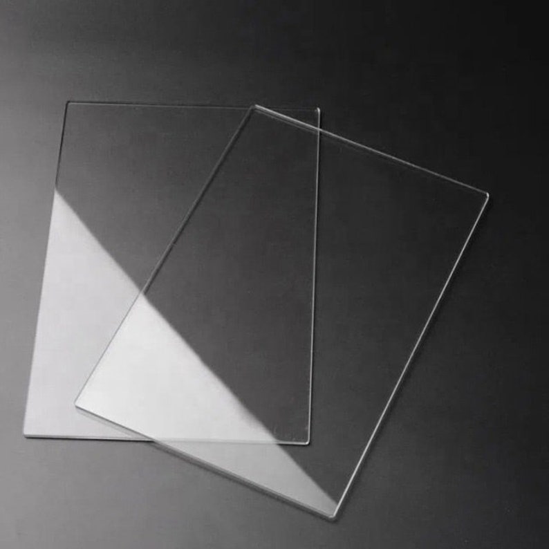 May include: Two clear acrylic sheets, one slightly larger than the other, are stacked on top of each other. The sheets are smooth and translucent, with a slight sheen.