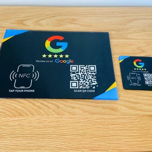 May include: Black and yellow sign with a Google logo, five stars, and the text "Review us on Google". The sign also includes a QR code and a symbol for NFC, with the text "TAP YOUR PHONE" and "SCAN QR CODE".