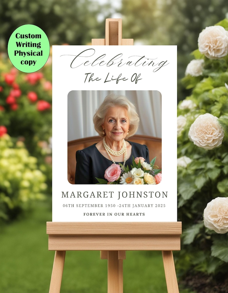 May include: A white easel with a white sign that says "Celebrating The Life Of" with a photo of a woman holding flowers. The text below the photo says "Margaret Johnston 06th September 1950 - 24th January 2025 Forever In Our Hearts."