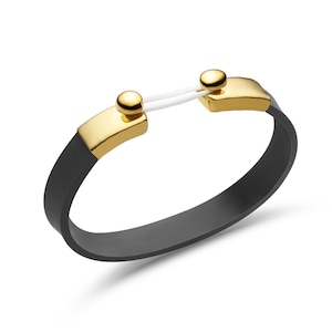May include: A black bracelet with gold-colored accents. The bracelet features a gold-colored clasp with a white cord connecting the two sides. The band of the bracelet is black and has a smooth finish. The bracelet is shown against a white background.