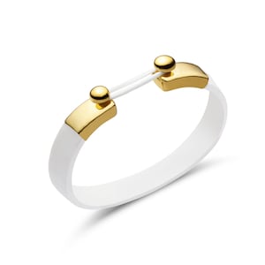 May include: White silicone bracelet with gold-colored metal accents. The bracelet features a curved design with two gold-colored rectangular clasps and a connecting white cord. The gold clasps have a small, round gold stud on top.