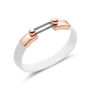 Puede incluir: Una pulsera de silicona blanca con detalles metálicos de color oro rosa. La pulsera presenta una barra gris que conecta los dos cierres de color oro rosa. El diseño es moderno y minimalista.
