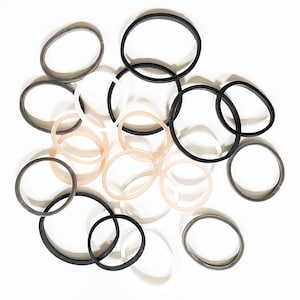 May include: A collection of rubber bands in various colours, including black, grey, white, and beige. The rubber bands are arranged in a random pattern on a white background.