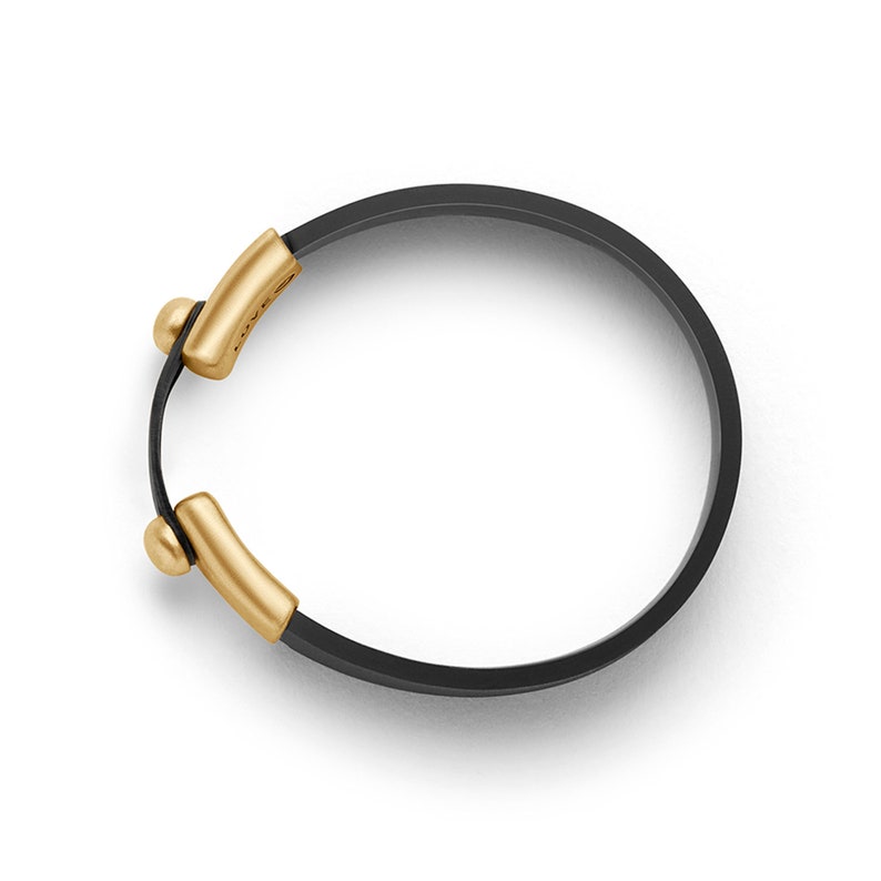Puede incluir: Un brazalete de cuero negro con detalles dorados. El brazalete tiene un dise&ntilde;o sencillo y es ajustable.