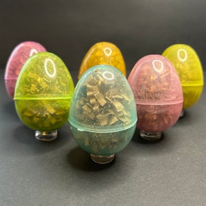 May include: Six colorful plastic eggs with a confetti-like filling. The eggs are in various shades of pink, yellow, green, and blue.