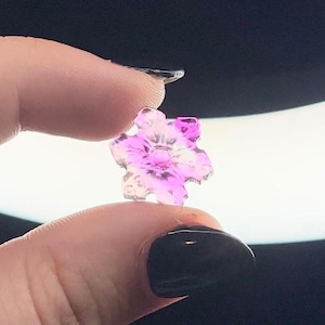 May include: A pink and white snowflake-shaped crystal charm with a clear center.