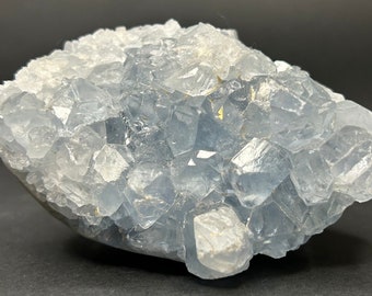 May include: A cluster of light blue celestite crystals with a rough, natural texture. The crystals are clustered together in a random, organic pattern.