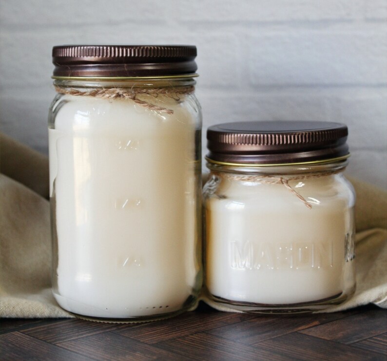 May include: Two glass candle jars with brown lids and a white candle inside. The larger jar has markings on the side.