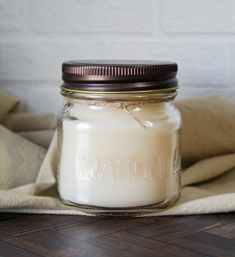 May include: A clear glass jar candle with a brown metal lid and a white wax candle inside. The jar has the word "MARTINI" embossed on the side.