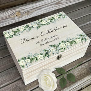 May include: A white wooden keepsake box with a floral design and the text "Thomas & Katherine - Mr & Mrs Arthur - 11th March 2025".