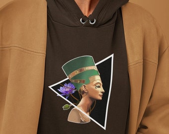 Pode incluir: Um moletom marrom escuro com um gráfico de uma mulher com um cocar verde e uma flor roxa, dentro de um triângulo branco. A pessoa está usando uma jaqueta bege e segurando um origami de pássaro.