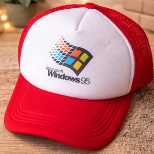 Könnte beinhalten: Rote und weiße Trucker-Cap mit dem Microsoft Windows 95 Logo. Die Cap hat einen roten Schirm und eine Netzrückseite, mit dem Windows 95 Logo auf der weißen Frontplatte. Das Logo zeigt die Windows-Flagge und den Text "Microsoft Windows 95".