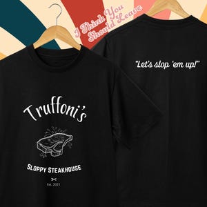 Può includere: Maglietta nera con una grafica bianca di una bistecca e il testo "Truttoni's Sloppy Steakhouse Est. 2021". Il retro della maglietta ha il testo "Let's slop 'em up!"