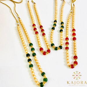 May include: Three strands of pearl necklaces with alternating green and red beads. The necklaces are made of faux pearls and have a gold finish.