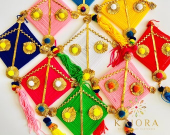 May include: A set of nine colorful diamond-shaped wall hangings made of yarn and decorated with gold accents. Each hanging features a tassel and pom-poms. The hangings are arranged in a staggered pattern on a white background. The text "KAHORA THE HOUSE OF HAPPINESS" is visible in the bottom right corner of the image.