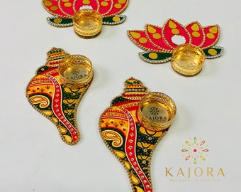 May include: Four decorative candle holders, two in the shape of a conch shell and two in the shape of a lotus flower. The holders are painted in vibrant colors with gold accents and feature intricate designs. The word "Kajora" is printed on the holders.
