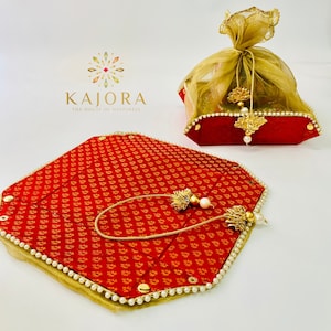 Pu&ograve; includere: Due vassoi decorativi rossi e dorati con bordo di perle. I vassoi sono decorati con un motivo floreale e hanno un fiocco dorato appeso a ciascuno. Il testo "KAIORA THE HOUSE OF HAPPINESS" &egrave; stampato nella parte superiore dell'immagine.