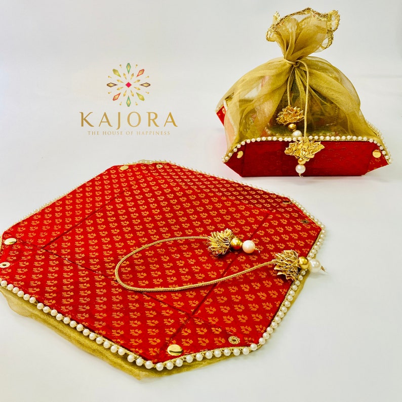 Pu&ograve; includere: Due vassoi decorativi rossi e dorati con bordo di perle. I vassoi sono decorati con un motivo floreale e hanno un fiocco dorato appeso a ciascuno. Il testo "KAIORA THE HOUSE OF HAPPINESS" &egrave; stampato nella parte superiore dell'immagine.
