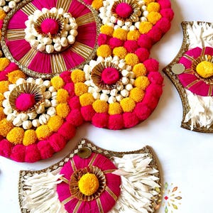 May include: A set of decorative wall hangings made with pink, yellow, and white pom-poms and fabric. The hangings are in the shape of a circle, a crescent moon, and a half-moon. The text "Kajora House of Happiness" is visible in the bottom right corner of the image.