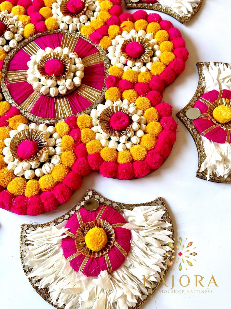 May include: A set of decorative wall hangings made with pink, yellow, and white pom-poms and fabric. The hangings are in the shape of a circle, a crescent moon, and a half-moon. The text "Kajora House of Happiness" is visible in the bottom right corner of the image.