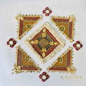 May include: A set of five gold and red decorative wall hangings with intricate designs and embellishments. The hangings are arranged in a square pattern with a white square in the center. The white square has a gold and green design with a fringe border. The hangings are surrounded by four small red square candle holders.
