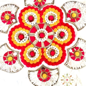 May include: A decorative wall hanging made of white, red, and yellow pom-poms arranged in a circular pattern. The center of the hanging features a red and gold circle with a white pom-pom in the center. The hanging is surrounded by six white, red, and yellow fan-shaped pieces.
