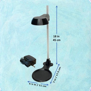 May include: Black desk lamp with a circular base, measuring 4 1/4 inches / 11 cm wide and 7 inches / 17.5 cm long. The lamp is 18 inches / 45 cm tall. Includes a power adapter.