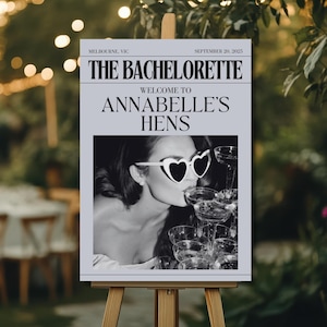 以下が含まれることがあります： ハート型のサングラスをかけ、シャンパンを飲む女性の白黒写真。写真は「The Bachelorette」と「Welcome to Annabelle's Hens」と書かれた看板に飾られています。