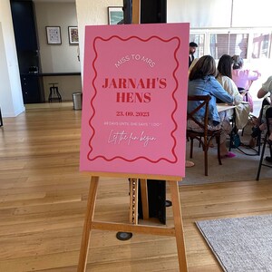 May include: Pink sign with white text announcing a bridal shower for Jarna, with the date 23.09.2023 and the phrase "Let the fun begin".