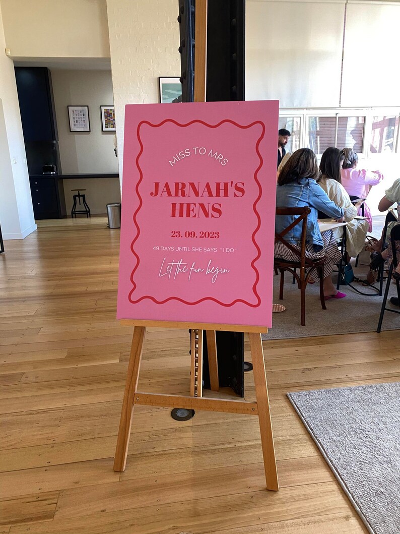 May include: Pink sign with white text announcing a bridal shower for Jarna, with the date 23.09.2023 and the phrase "Let the fun begin".