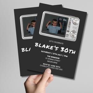 May include: A black invitation card featuring a silver digital camera graphic with a photo of a child in a striped shirt. The text reads: LET'S CELEBRATE BLAKE'S 30TH, SATURDAY | 27TH JULY | 7PM, THE WINDSOR, 111 SPRING STREET, MELBOURNE, RSVP BY JUNE 30TH.