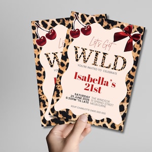 May include: Two party invitations with a leopard print border and a light pink center. The invitations read "Let's Get WILD" and "Isabella's 21st". Red cherries and a red bow are featured on the invitations.