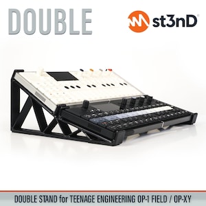 Op de afbeelding: Een zwart-witte dubbele standaard voor een Teenage Engineering OP-1 Field / OP-XY. De standaard is schuin en heeft een toetsenbordachtig oppervlak met diverse knoppen en knoppen. Het woord 'DOUBLE' staat bovenaan afgedrukt.