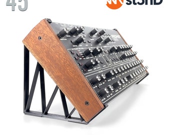 May include: A wooden stand with a black metal frame, designed to hold a Sequential Prophet Rev2 synthesizer at a 45-degree angle. The stand is labelled "st3nD" and "STAND for SEQUENTIAL PROPHET REV2 - 45° - st3nD".