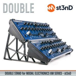 May include: A double stand for Modal Electronics 8M series synthesizers. The stand is black and supports two blue synthesizers. The word "DOUBLE" is in large gray letters at the top. The st3nD logo is in the upper right corner.