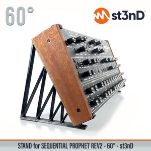 Può includere: Un sintetizzatore nero e argento con un supporto in legno. Il supporto è inclinato di 60 gradi. Il sintetizzatore ha un'etichetta che dice "Sequential Prophet Rev2". Il supporto è etichettato "st3nD".