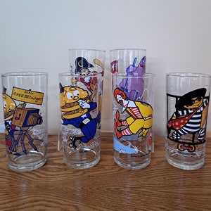 May include: Set of six vintage McDonald's glasses featuring various characters including Ronald McDonald, Grimace, and the Hamburglar. The glasses are clear with colorful cartoon illustrations and the text "Say Cheeseburger" on one glass.