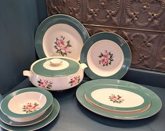 May include: A set of vintage green and white floral china dinnerware. The set includes a large serving bowl with a lid, a large dinner plate, a smaller salad plate, a soup bowl, and a serving platter. The floral design features pink flowers with green leaves.