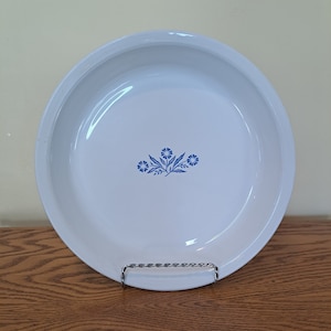 May include: White pie plate with a blue floral design. The design features a cluster of five blue flowers with green leaves.