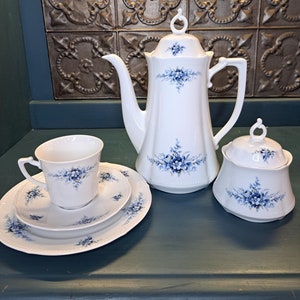 May include: A white tea set with blue floral designs. The set includes a teapot, sugar bowl, creamer, and a cup and saucer.
