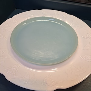 May include: A white plate with a raised grape design and a light blue plate on top.