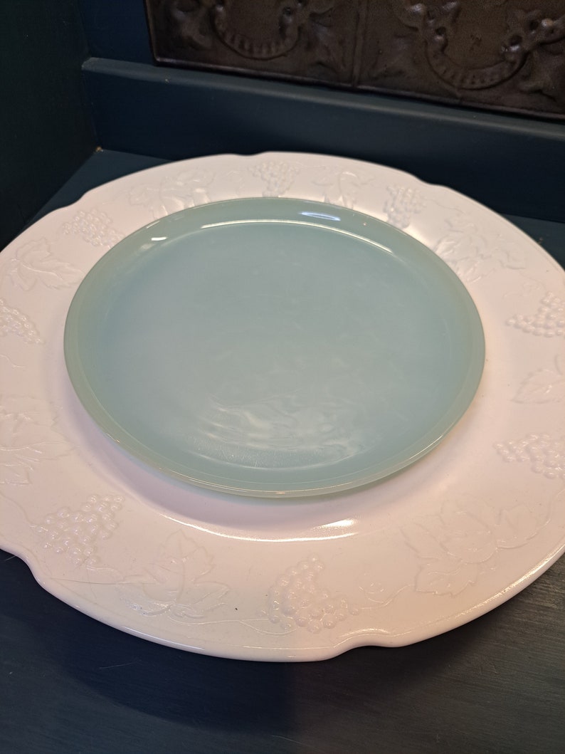 May include: A white plate with a raised grape design and a light blue plate on top.