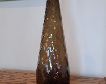 May include: A tall, brown glass bottle with a twisted design. The bottle has a wide mouth and a narrow neck.