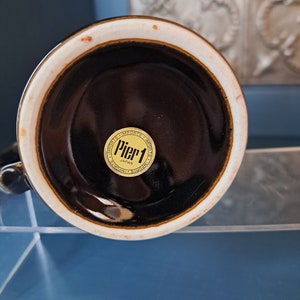 May include: The bottom of a brown ceramic mug with a gold sticker that reads "Pier 1 Imports Japan".