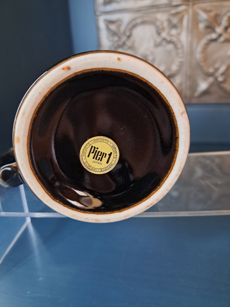 May include: The bottom of a brown ceramic mug with a gold sticker that reads "Pier 1 Imports Japan".