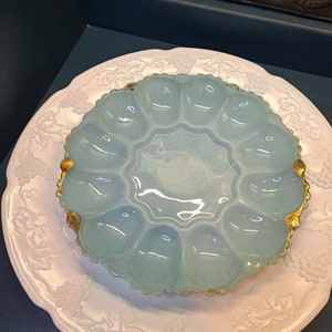 May include: A light blue glass egg plate with a gold rim, sitting on a white plate with a grapevine design.
