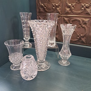 May include: Five clear glass vases with a diamond pattern. The vases are arranged on a teal surface.