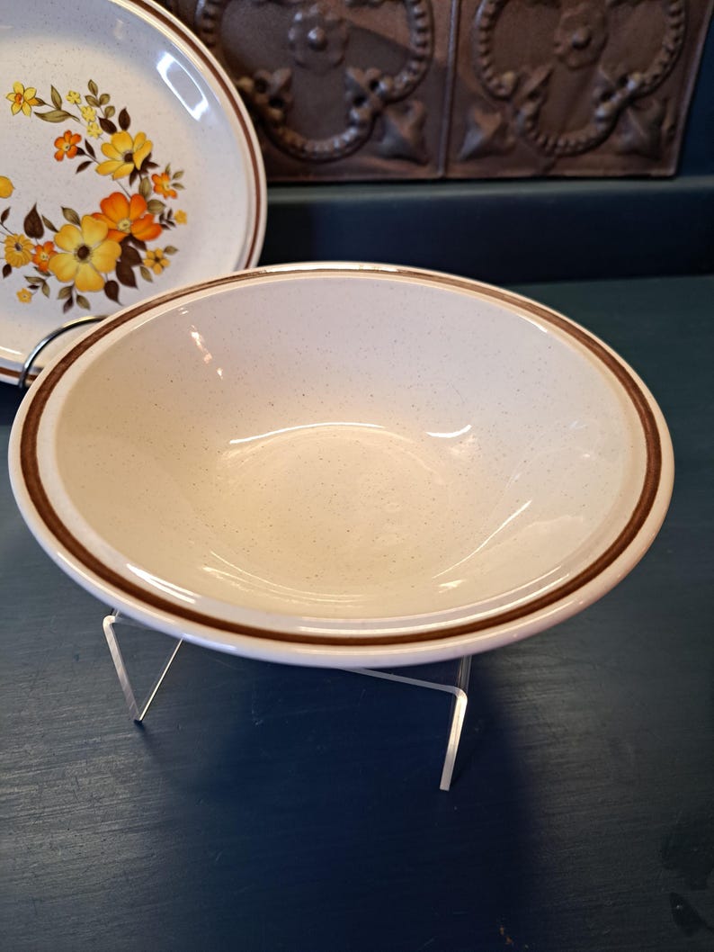 May include: A white ceramic bowl with a brown rim. The bowl has a speckled texture and is sitting on a blue surface.